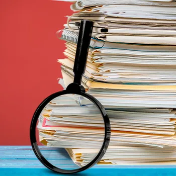 Magnifying glass standing beside a stack of documents and files