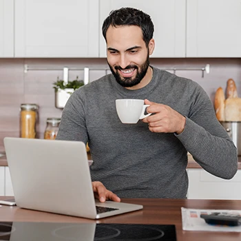 A man drinking coffee while checking if a name is trademarked using a laptop